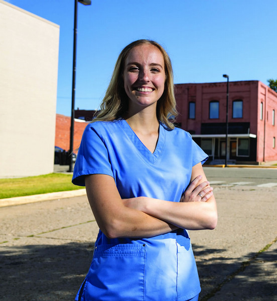 Scholarship receiptient and dental student Katie Roe stands with her arms crossed and dressed in scrubs in front of rural dentistry practice.