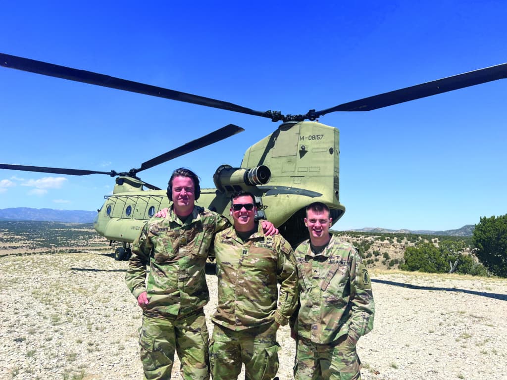 three soldiers posing in front of helicopter