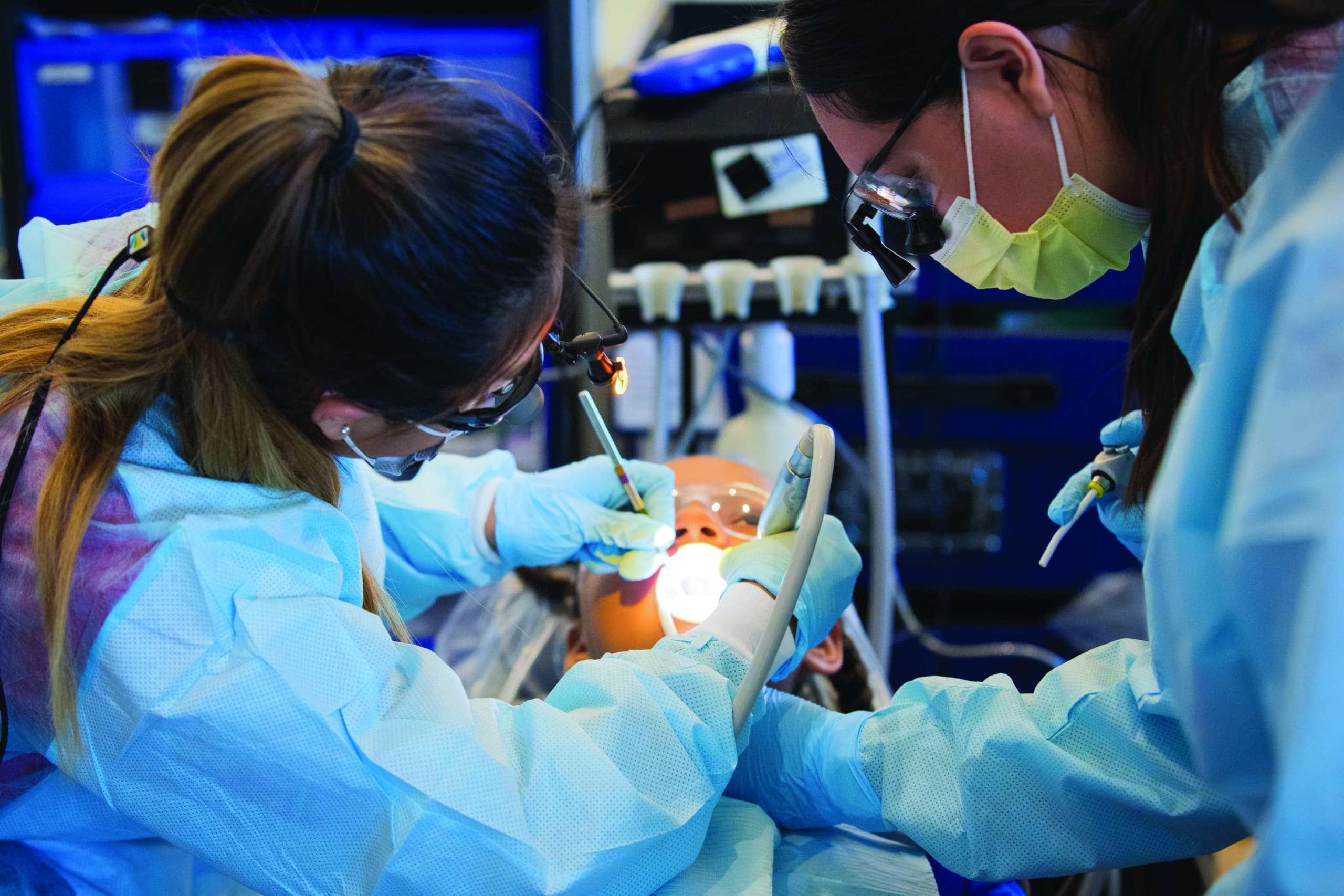 Students in scrubs and mask operating on patient in chair