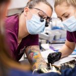 Dental hygiene student Macila Arnold wears a mask and face shield while cleaning the teeth of a primate at the zoo. She works with another student.